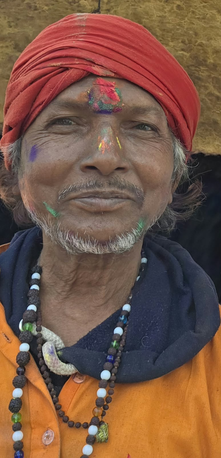 An elderly sadhu with Holi colours on his face and a red turban