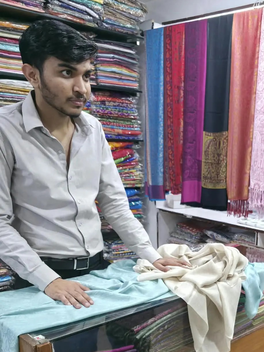 A shopkeeper presenting handwoven textiles in his shop